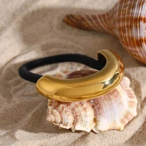 18k gold curved metal hair tie cuff close-up top-down beach sand background luxury