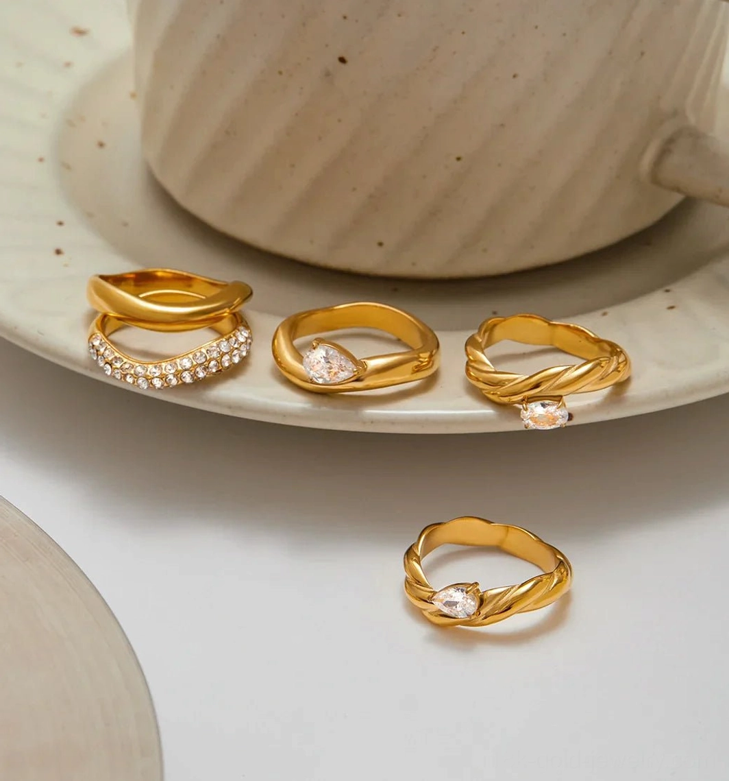 Studio flat lay of assorted 18K gold rings with pavé bands and twist solitaire designs