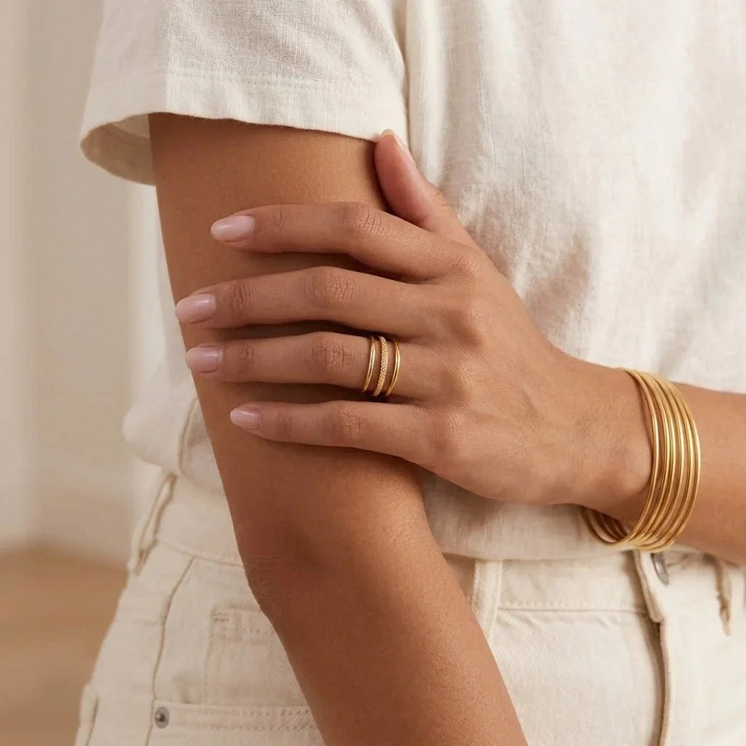 Gold bangle bracelet with matching thin ring on model's hand and wrist