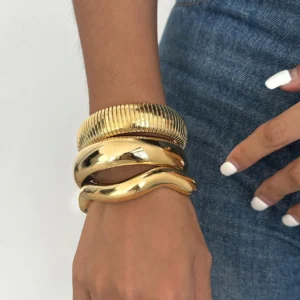 Stacked 18K gold chunky bangles on wrist featuring ribbed textured and smooth polished designs, styled with denim