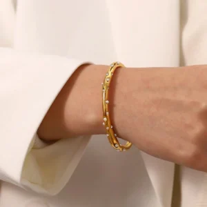 18K gold bangle worn on female wrist, close-up side view showing asymmetrical gem arrangement and fit on slim wrist
