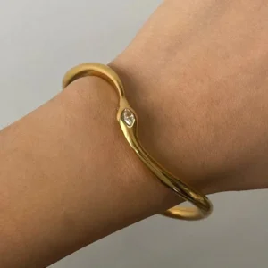 18K gold open cuff bangle worn on light-toned wrist, close-up side view showcasing smooth gold surface and embedded crystal detail