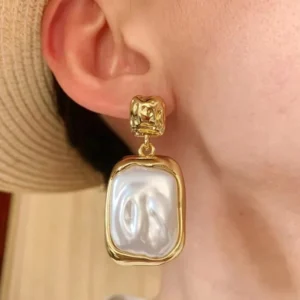 Single baroque pearl drop earring worn on ear showing glossy freshwater pearl in gold bezel setting close-up detail