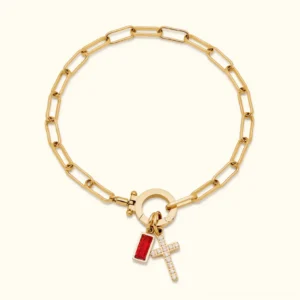 18K gold birthstone cross charm bracelet with red baguette gem and pavé cross charm on paperclip chain, flat lay product photography