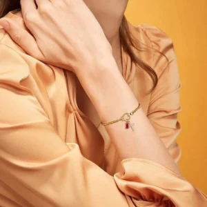 Birthstone cross bracelet worn on wrist close-up, modeling 18K gold beaded chain with pink gemstone charm and pavé cross pendant