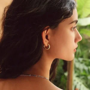 18K gold chunky hoop earrings worn on female model ear profile close-up with green plant background outdoor styling