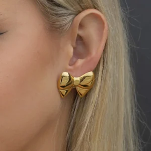 18K gold bow stud earring worn on ear close-up side view, showing elegant design on model with blonde hair
