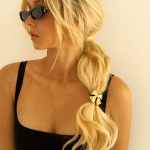 18K gold bow hair cuff worn on blonde woman's low ponytail, side view showcasing luxurious golden bow detail on black hair band