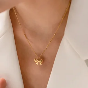 Delicate 18K gold bow necklace worn on neck close-up - female model wearing white blazer, showcasing dainty bow charm and satellite chain