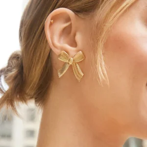 18K gold bow earrings worn on ear model close-up, side view showing textured ribbed design and comfortable fit