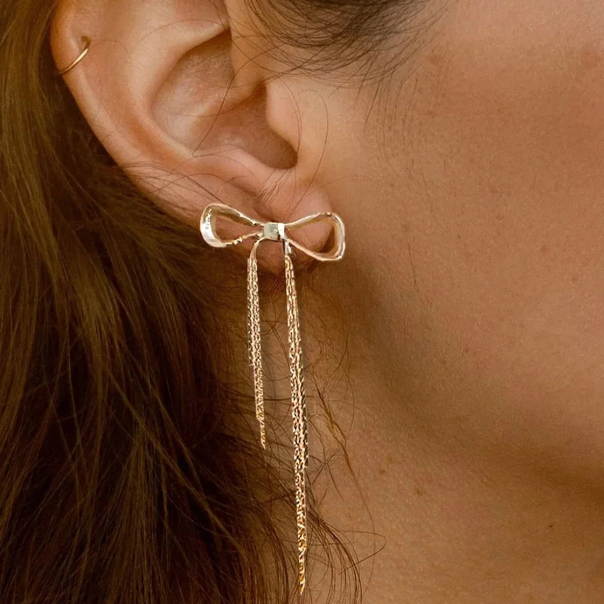 Gold bow earrings worn on model, close-up side profile showing dangling tassel chain length and gold tone