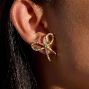Gold bow tie earrings on ear close-up side view worn by woman with dark hair diamond simulant details
