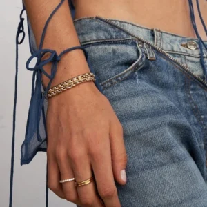 Gold curb chain bracelet worn on wrist with stacked rings casual denim styling layered jewelry look