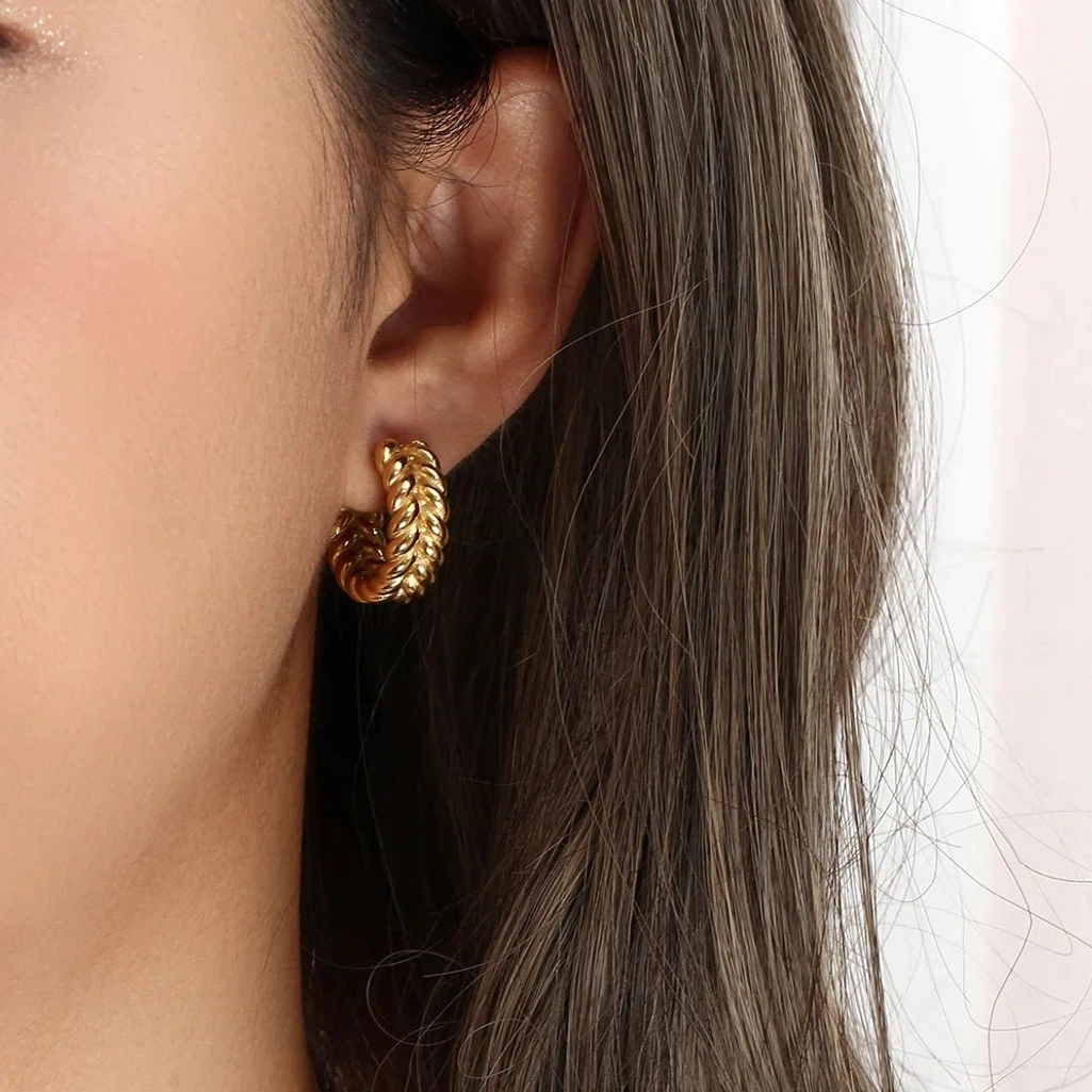 Close-up side ear view of 18K gold braided hoop earrings on model with long brown hair displaying fitted design warm golden tone
