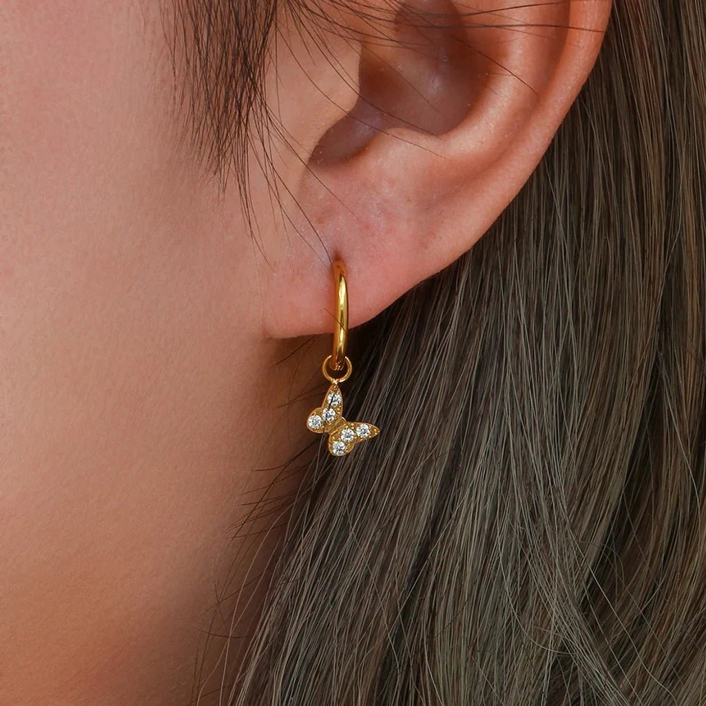 Woman modeling single 18K gold butterfly drop huggie earring close-up side view on ear