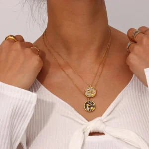 Layered 18K gold celestial necklaces worn on model's neck with white ribbed top and rings, lifestyle close-up