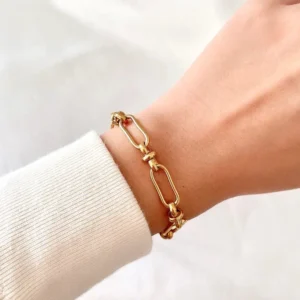 Gold paperclip bracelet worn on wrist, close-up side view with cream knit sleeve background showing perfect fit