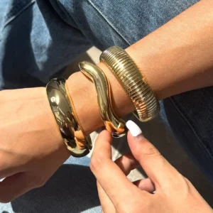 Three distinct 18K gold bangle styles worn together on wrist, side view showing twisted wavy and ribbed textures with high polish finish