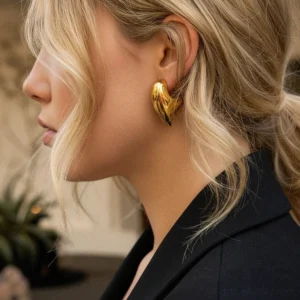 18K gold chunky heart earrings side profile close-up fitted on earlobe smooth solid gold texture model wearing black blazer