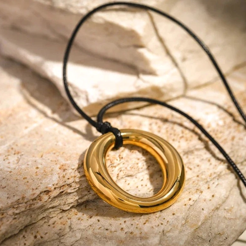 18K gold open circle pendant necklace close-up high angle view of glossy polished gold ring pendant with black necklace cord detail