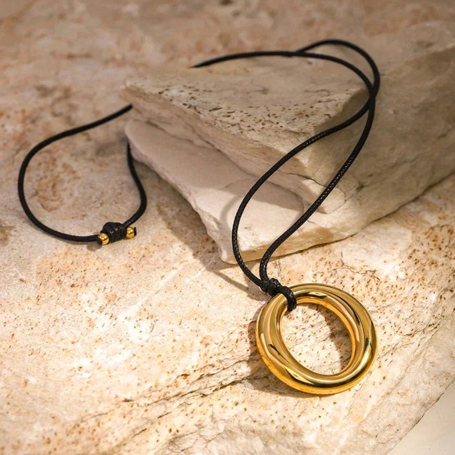 18K gold open circle pendant necklace side view showing adjustable black waxed cord with warm gold tone and natural stone texture background