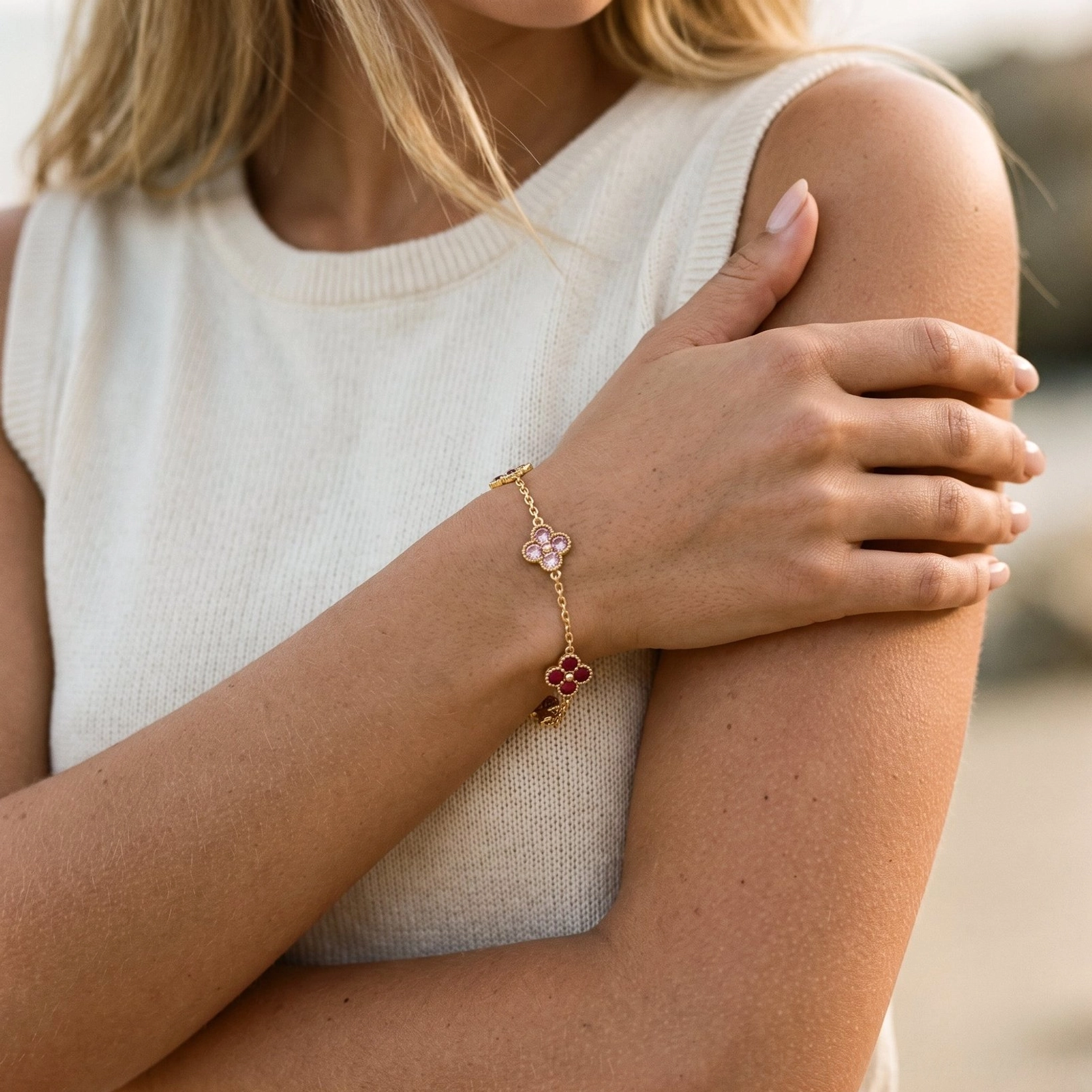 Woman wearing delicate four-leaf clover bracelet with pink and red gemstone charms on wrist, lifestyle photography