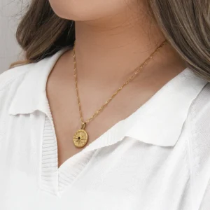 18K gold compass medallion necklace worn on model neck close-up styled with white collared knit top elegant positioning