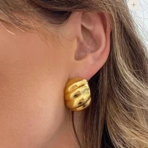 18K gold huggie earrings worn on female model's ear, side close-up view showcasing textured ridged golden surface and secure fit