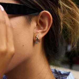 Two-tone cross huggie earrings worn on model's ear, side close-up showing fitted huggie style with mixed metal dual-tone finish