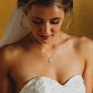 delicate gold cross pendant necklace worn by bride on collarbone with wedding dress close-up detail shot