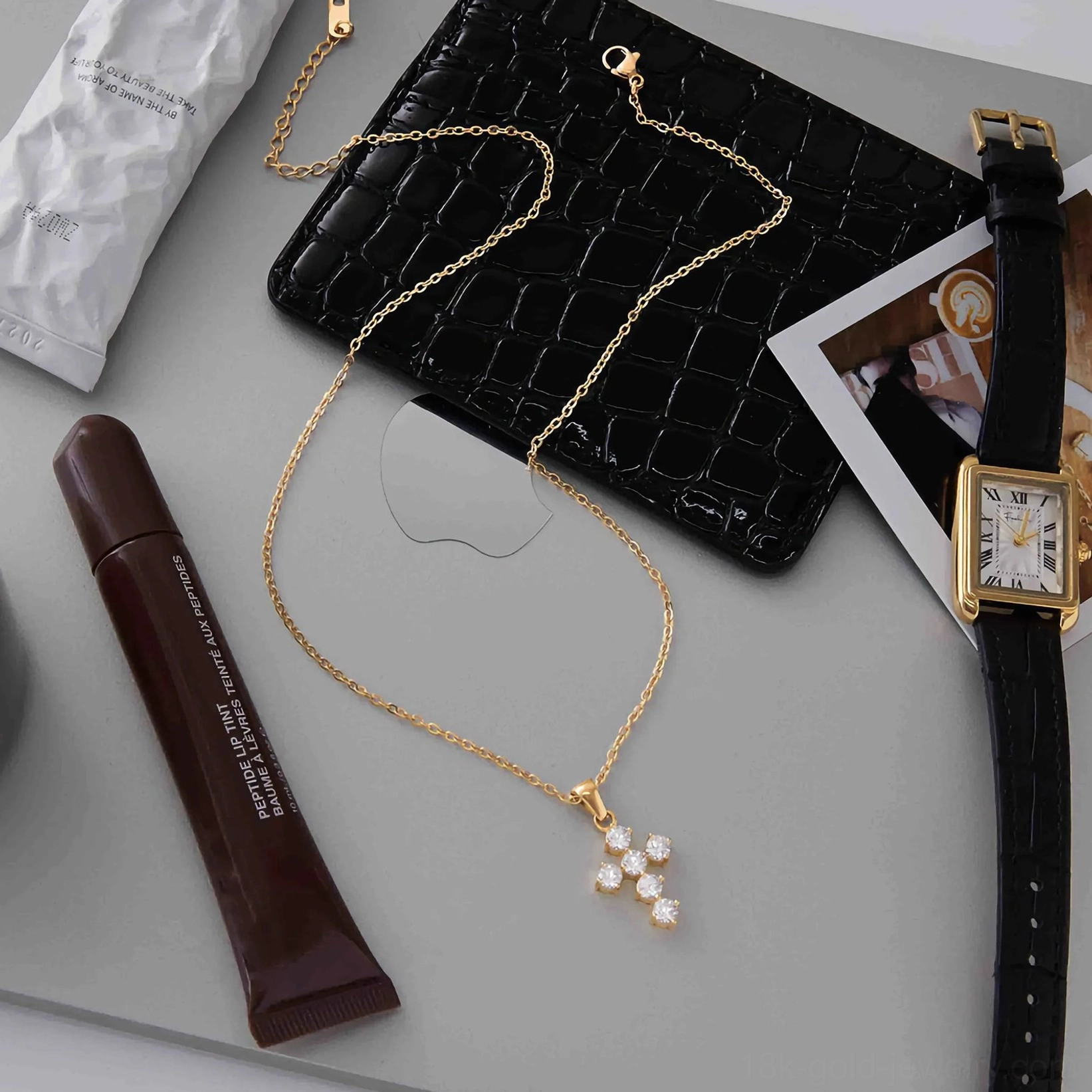 styled 18k gold cross necklace jewelry flat lay with leather bag and cosmetics daily accessory arrangement