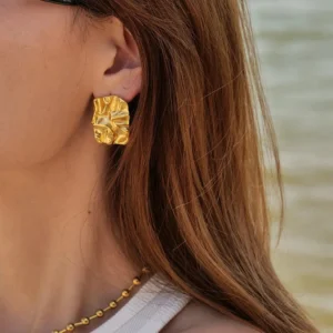18K gold crumpled stud earrings worn on ear close-up side view worn by female model seaside background