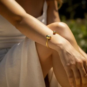 18K gold open cuff bracelet close-up side view worn on female wrist with white slip dress, showing slim elegant band design