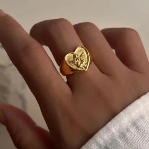 18K gold cupid heart ring worn on hand, middle finger, showing warm gold tone and detailed angel engraving in on-body styling