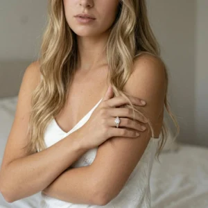 Woman wearing 18K Gold oval CZ solitaire ring on left ring finger, styled with white camisole in bedroom setting, demonstrating elegant everyday wear