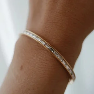 Close-up wrist shot of 18K gold bangle bracelet with baguette diamonds worn on brown skin tone