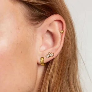 18K gold diamond earring bundle set worn on multiple ear piercings, featuring polished gold huggie hoops and crystal studs on light skin tone, lifestyle shot showcasing versatile layering