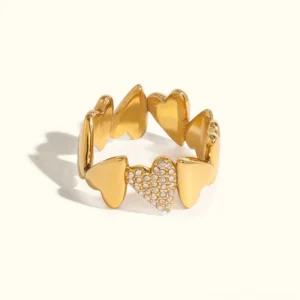 18K gold diamond hearts ring with central crystal-paved heart, flat lay studio view on off-white background showing linked heart design
