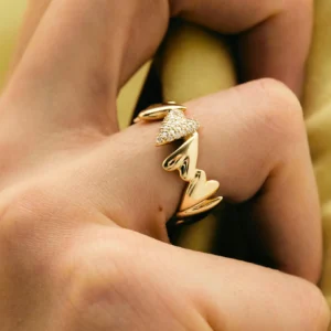 18K gold hearts ring worn on female hand with satin fabric background, close-up lifestyle shot showcasing crystal-studded centerpiece