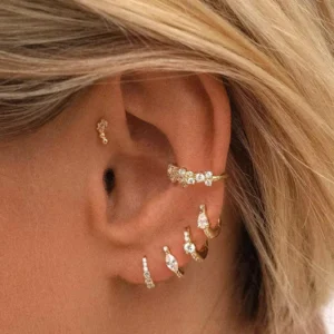 18K gold mini hoop earrings styled on ear, worn on blonde model demonstrating stackable cartilage piercing design with assorted gold-toned cubic zirconia jewelry