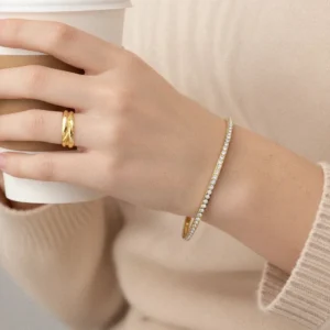 18K gold diamond bangle worn on wrist with twisted gold ring stacked together - styling detail on light skin tone showing elegant jewelry pairing