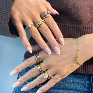 Mixed metal 18K gold diamond rings on hands - close-up wearing brown knit, French tip manicure with stacked gold and diamond bands
