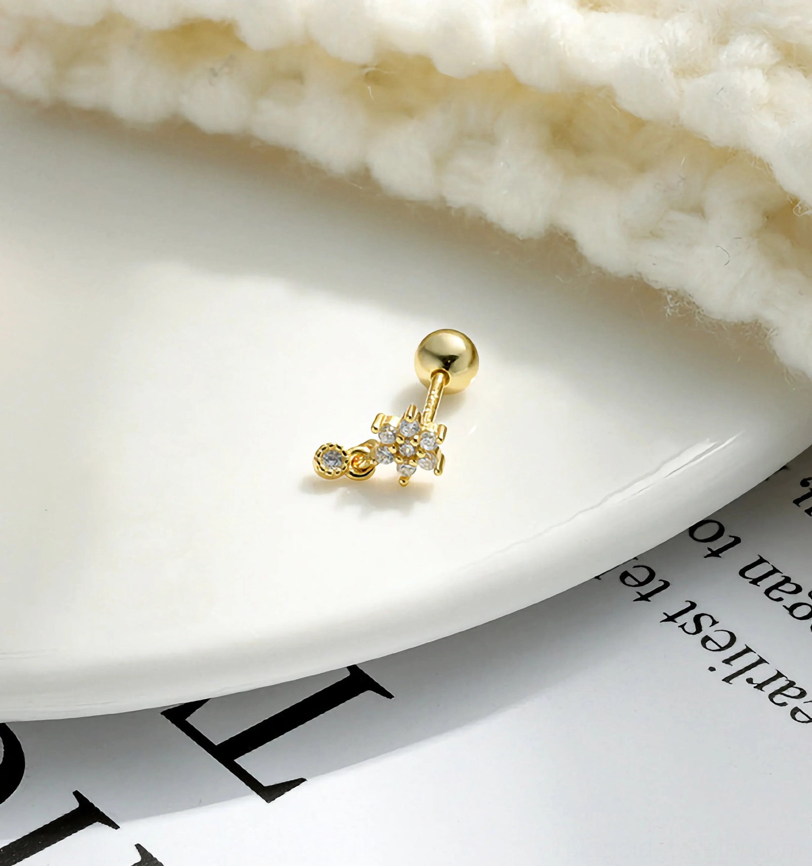 Mini gold cubic zirconia cartilage stud earring top-down flat lay on ceramic plate with knit fabric background