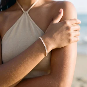 Woman wearing 18K gold diamond tennis bracelet on beach, halter top outfit, close-up wrist and shoulder styling inspiration