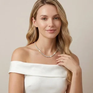 Blonde woman wearing elegant 18K gold tennis necklace with round diamond simulants on collarbone, off-shoulder white dress styling