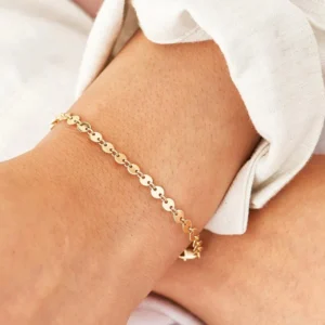 18K gold disc chain bracelet worn on female wrist close-up detail shot with white garment showing slim sleek gold tone links