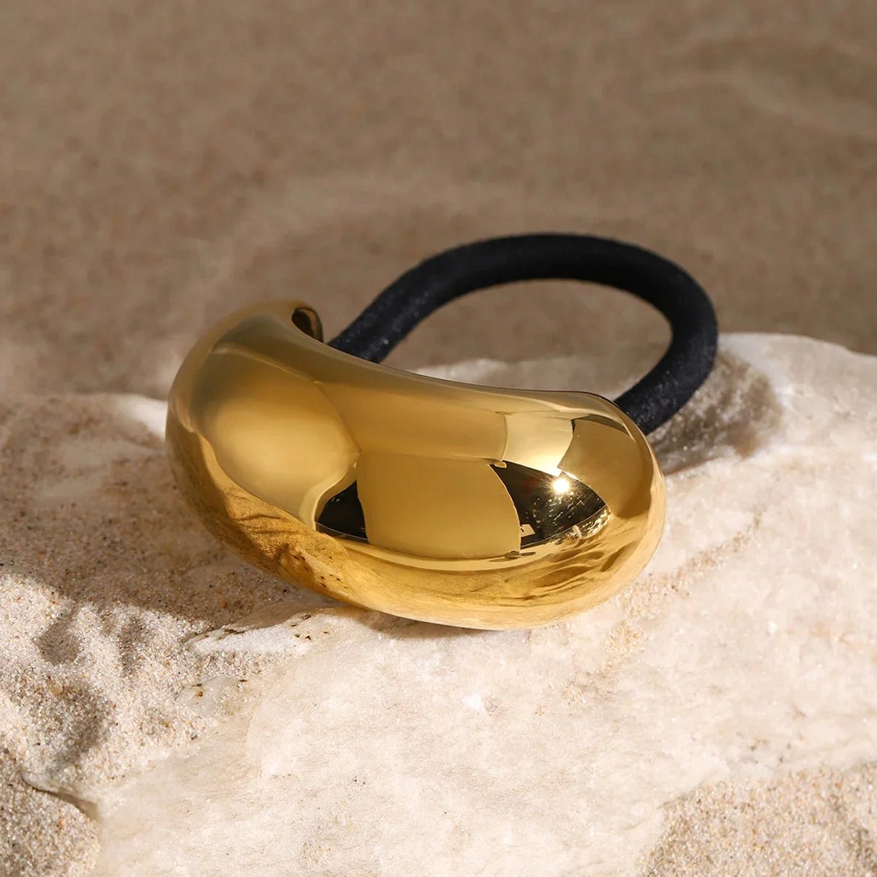 Gold dome hair cuff on beach sand background, smooth bean-shaped design side view