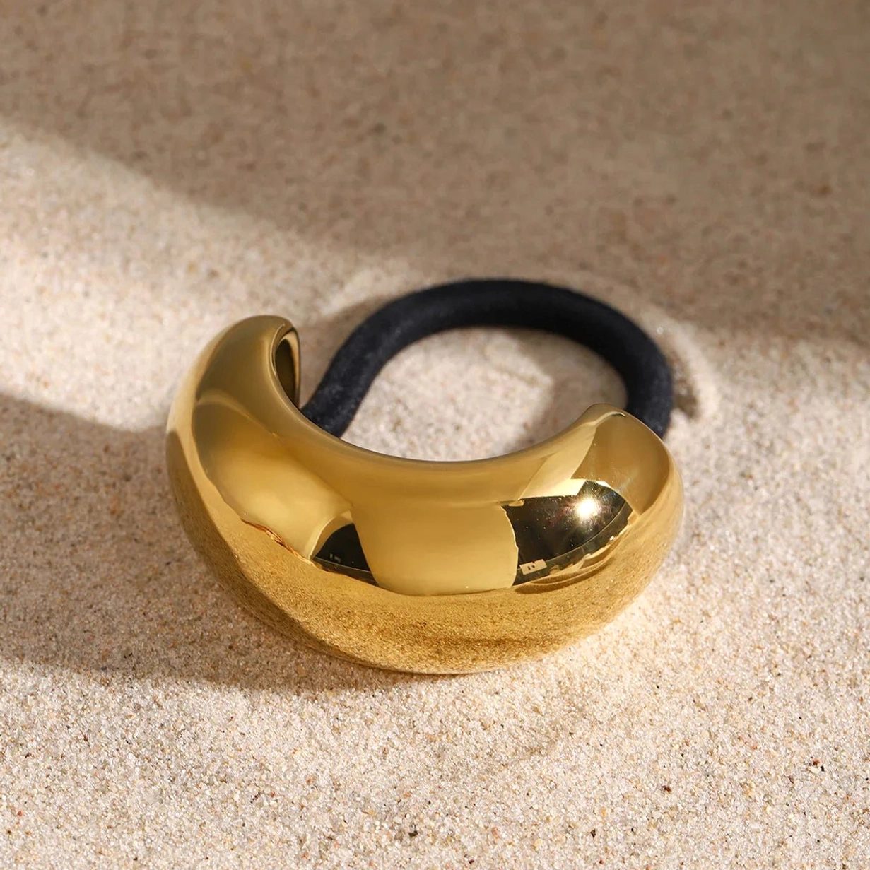 Glossy gold dome ponytail cuff front view beach sand background, polished metal surface
