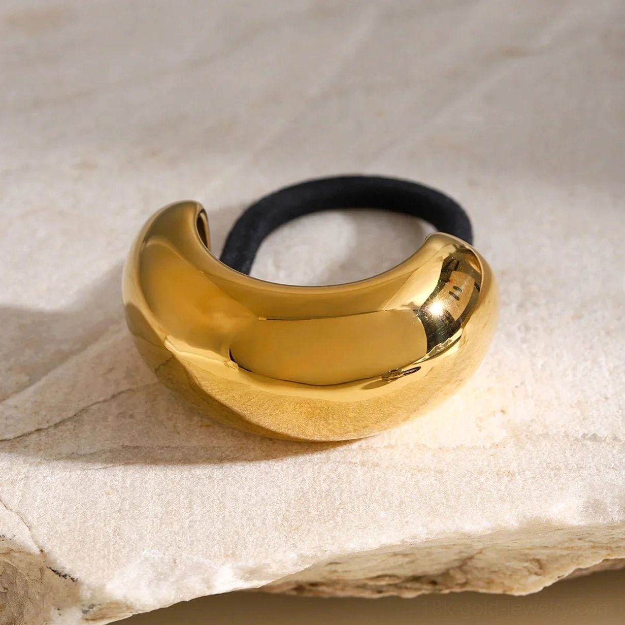 Gold dome hair cuff on sandstone slab background, glossy curved surface oblique view