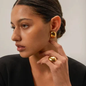 Woman wearing 18K gold dome ring on finger, paired with matching gold dome earrings, side profile studio portrait showing minimalist luxury jewelry styling